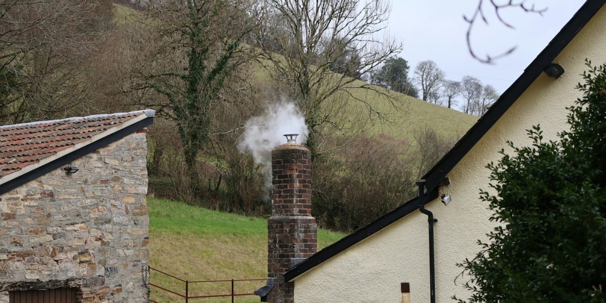 Smoke billowing from a brick chimney on a cloudy day.