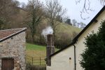 Smoke billowing from a brick chimney on a cloudy day.