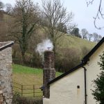 Smoke billowing from a brick chimney on a cloudy day.